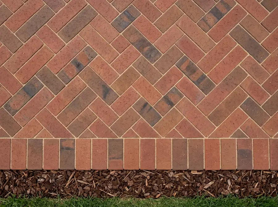 Top view of red-brown blend clay pavers laid in 45 degree herringbone against a border row