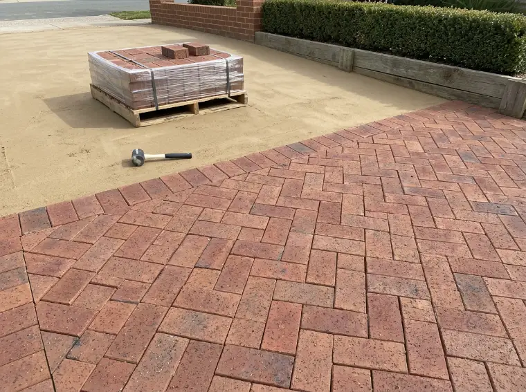 Clay pavers half laid in herringbone over screeded sand with a pallet of pavers