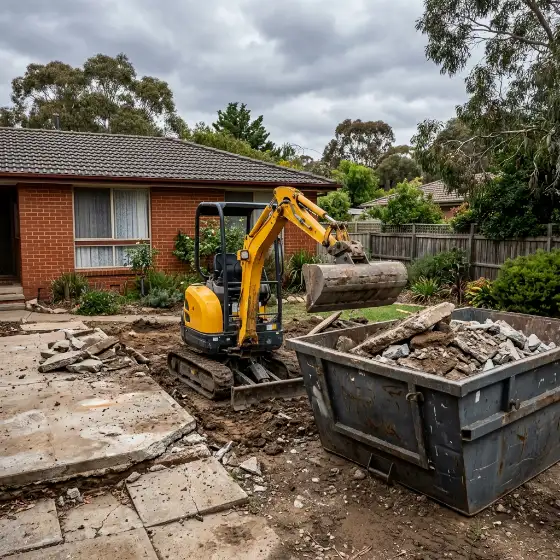 Small excavator lifting old concrete into a skip bin