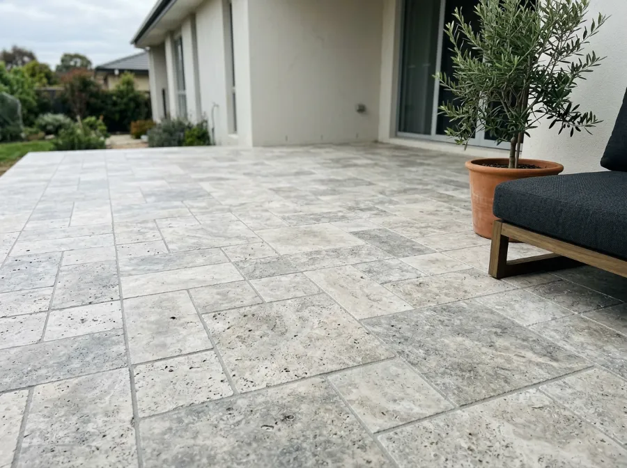 Honed silver travertine pavers laid in a French pattern on a backyard patio