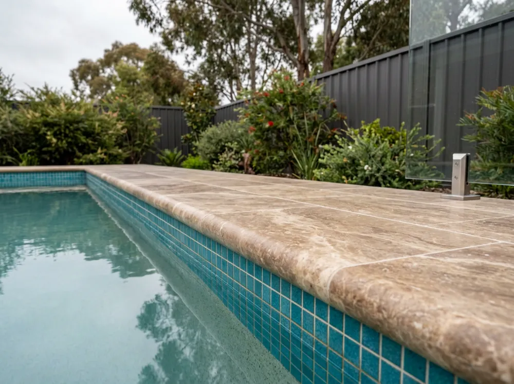 Filled walnut travertine bullnose coping with a smooth rounded front edge over a mosaic-tiled pool