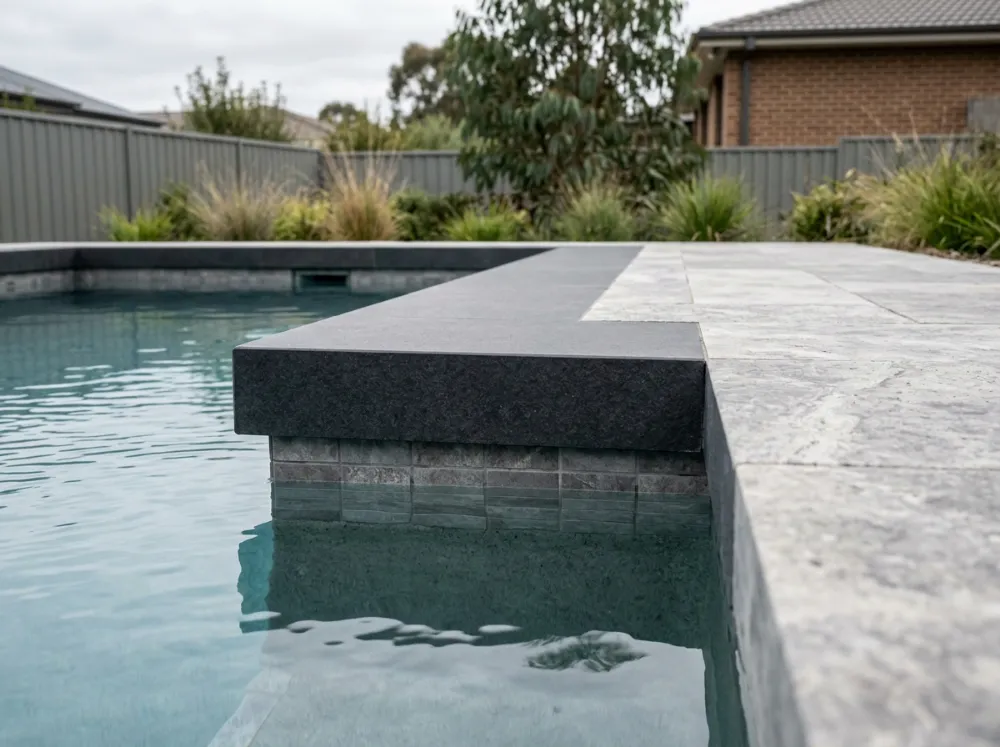 Charcoal porcelain drop face coping with a deep square front face over the pool tiles, beside a silver travertine surround