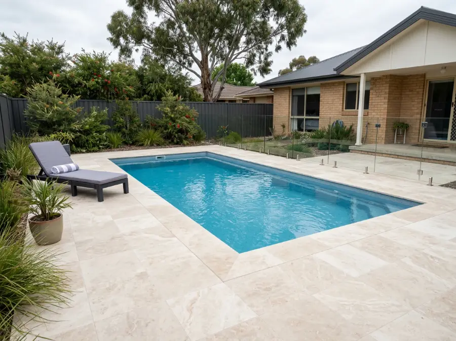 Filled and honed ivory travertine pool surround around a rectangular pool, with a lounger and a frameless glass fence