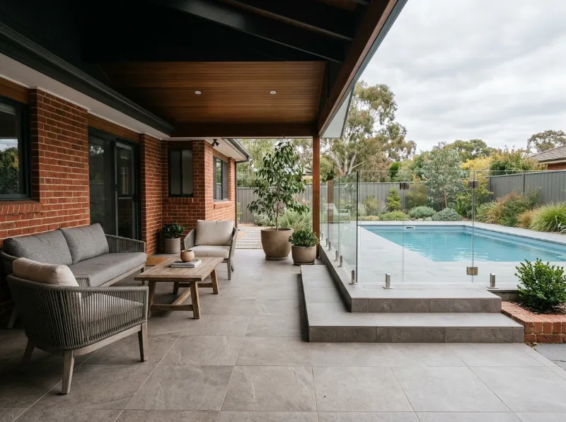 Covered alfresco tiled in large grey porcelain with a lounge setting, stepping down to the pool