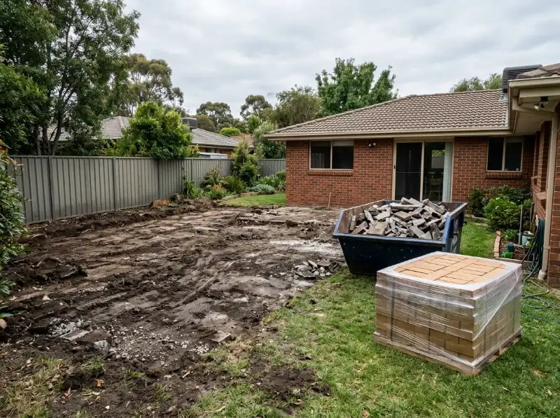 Old pavers removed to bare ground, with a skip of broken pavers and a pallet of new clay pavers on the lawn