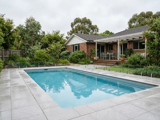 Backyard pool with a light grey porcelain surround and coping behind a Canberra brick home