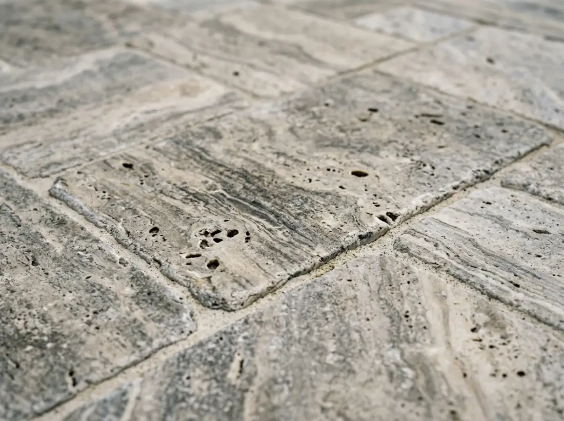 Close-up of silver tumbled travertine pavers showing natural holes, banding and colour variation